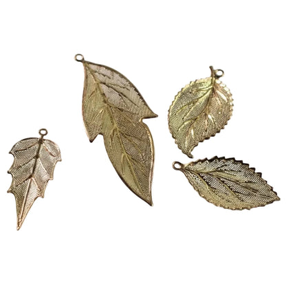Four gold-toned metal leaf-shaped charms with textured mesh details and small hanging loops, arranged on a plain white background.