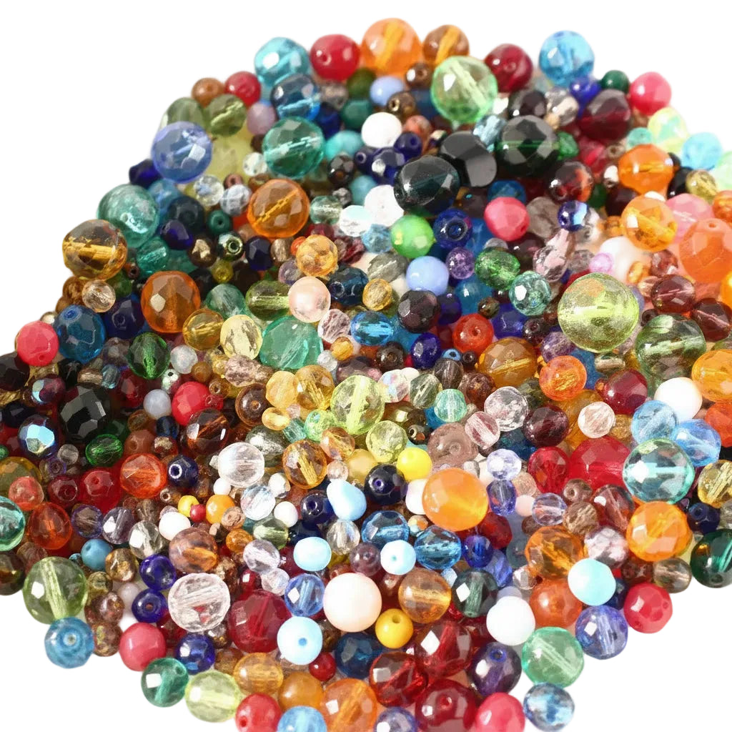 A close-up pile of colorful faceted glass beads in many shapes and sizes, including round, oval, and teardrop forms in red, orange, yellow, green, blue, purple, pink, and clear tones.