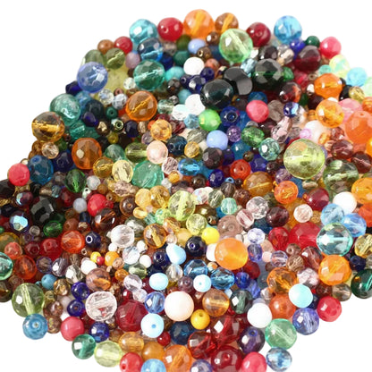 A close-up pile of colorful faceted glass beads in many shapes and sizes, including round, oval, and teardrop forms in red, orange, yellow, green, blue, purple, pink, and clear tones.