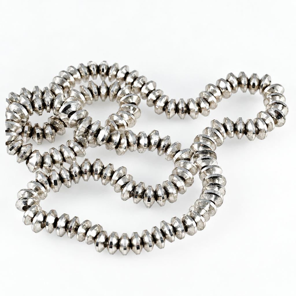 A close-up of a silver-toned beaded necklace made of small, faceted, spiral-shaped beads, arranged in loose loops on a plain white background.