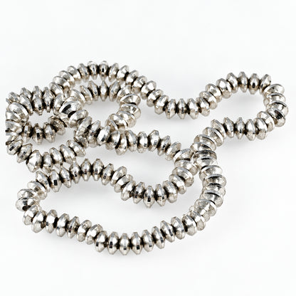 A close-up of a silver-toned beaded necklace made of small, faceted, spiral-shaped beads, arranged in loose loops on a plain white background.