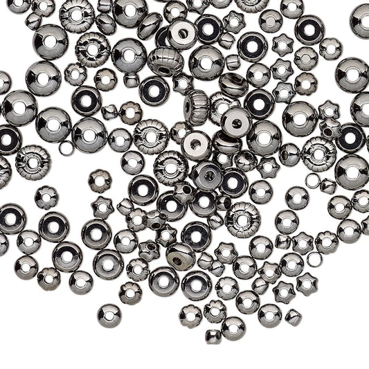 A pile of metallic gunmetal spacer beads in various shapes including round, star, and flower, scattered on a plain white background.