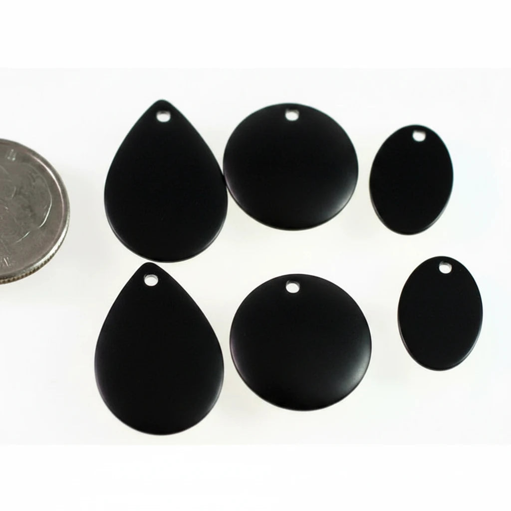 Six glossy black teardrop-shaped and oval jewelry charms with pre-drilled holes, arranged on a white background next to a silver coin for scale.