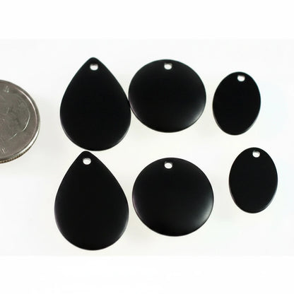 Six glossy black teardrop-shaped and oval jewelry charms with pre-drilled holes, arranged on a white background next to a silver coin for scale.