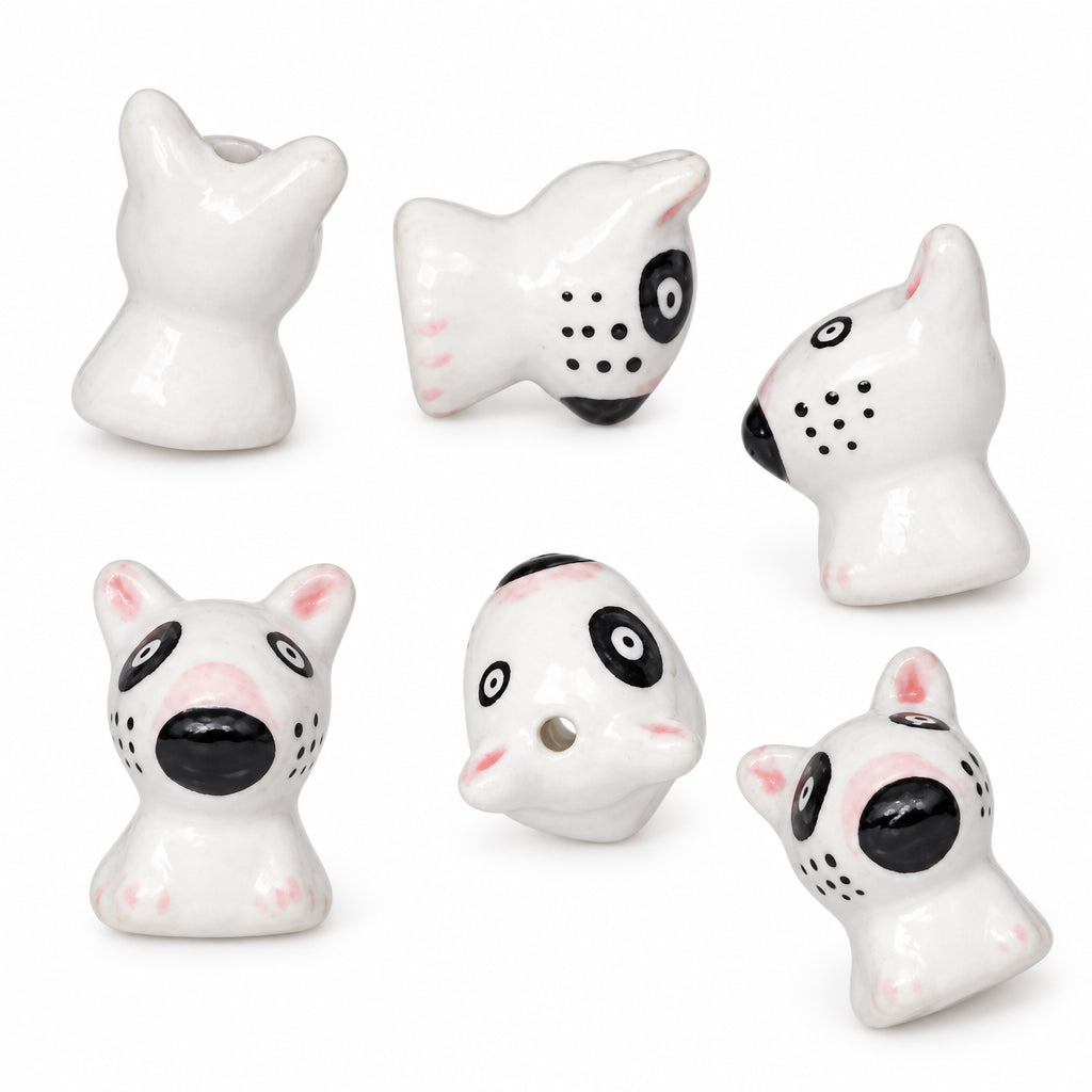 Six small white ceramic dog-shaped beads with black and pink details, arranged on a plain white background.
