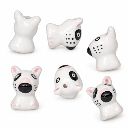 Six small white ceramic dog-shaped beads with black and pink details, arranged on a plain white background.