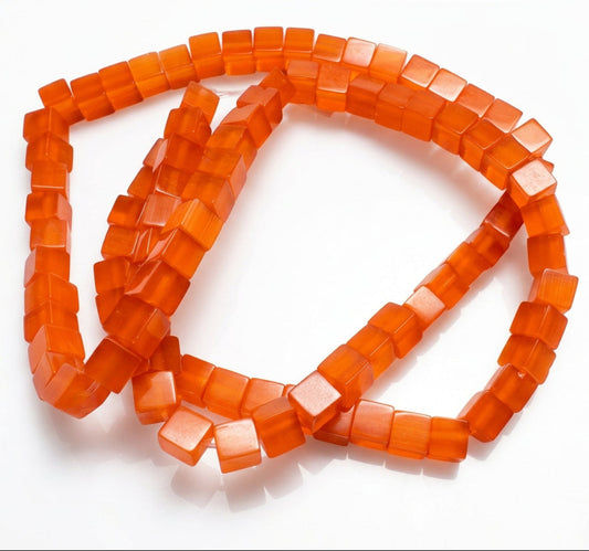 A coiled strand of translucent orange red square beads on a plain light gray background.