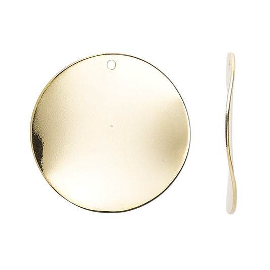 A blank round gold-tone metal disc pendant with a small hanging hole, shown next to a matching curved gold-tone tool on a plain white background.