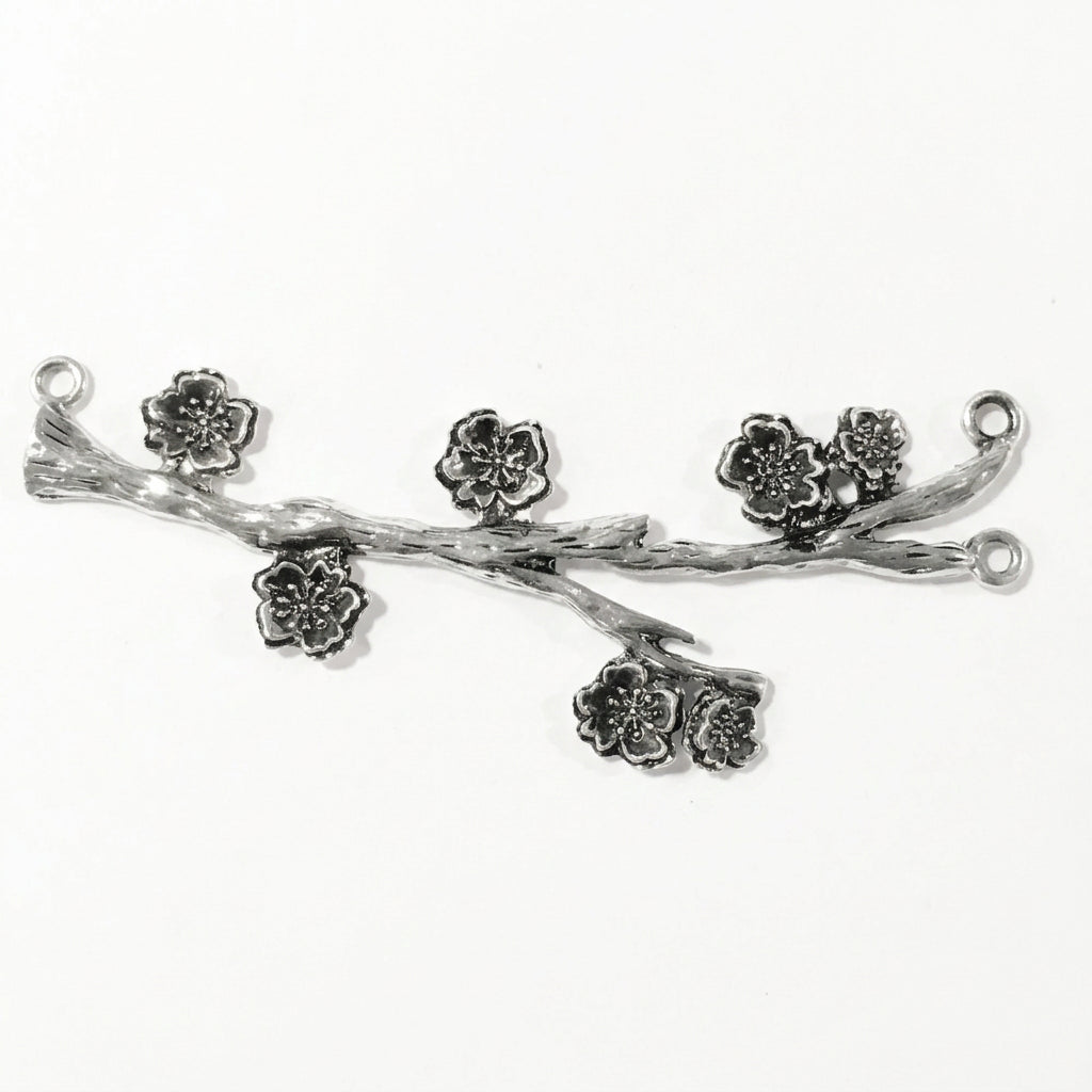 A silver-toned metal jewelry finding shaped like a branch with five detailed cherry blossom flowers, shown on a plain white background.
