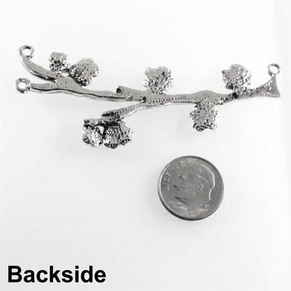 A silver-toned metal branch-shaped jewelry charm with textured leaf clusters and small hanging loops, shown on a white background next to a U.S.