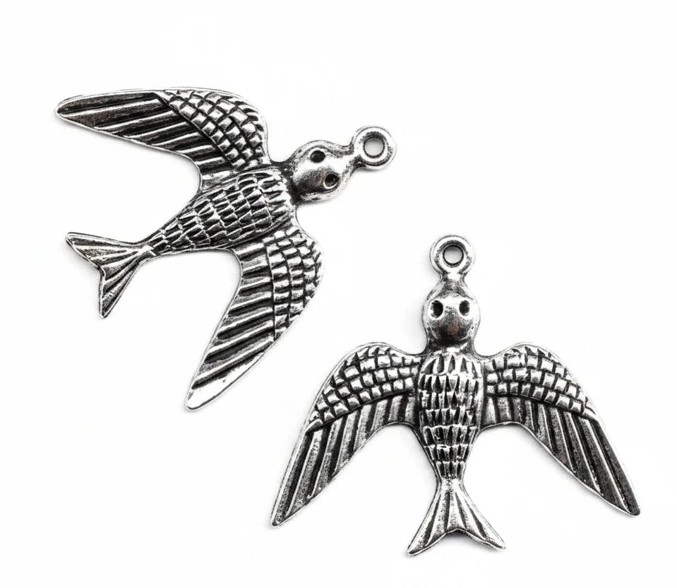 Silver-toned metal bird charms with detailed wing and body textures, shown on a plain white background with one charm fully visible and part of another at the bottom right.