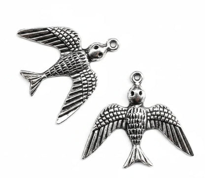Silver-toned metal bird charms with detailed wing and body textures, shown on a plain white background with one charm fully visible and part of another at the bottom right.