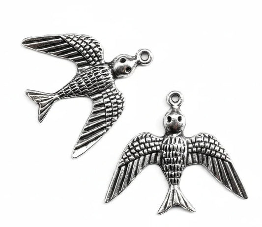 Silver-toned metal bird charms with detailed wing and body textures, shown on a plain white background with one charm fully visible and part of another at the bottom right.
