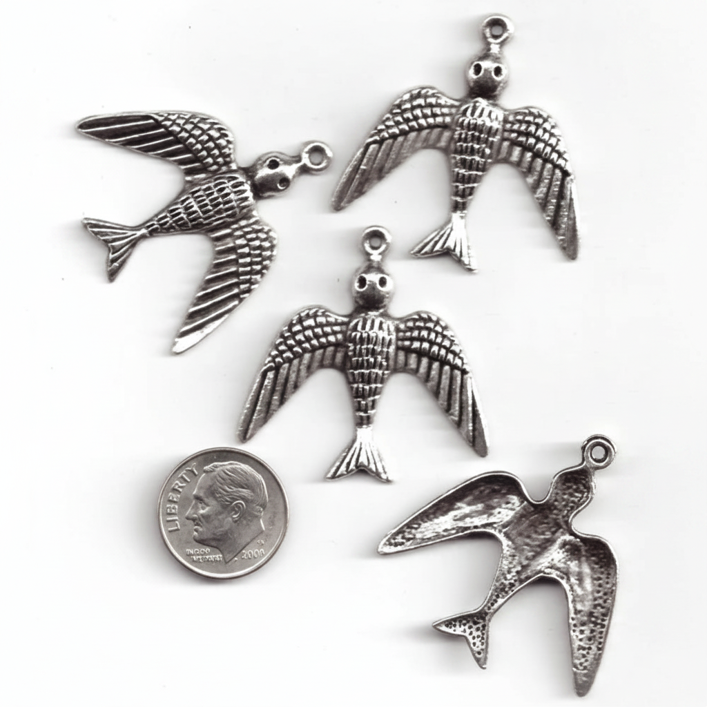 Four silver bird charms with wings spread, shown on a white background with a US quarter coin for scale.