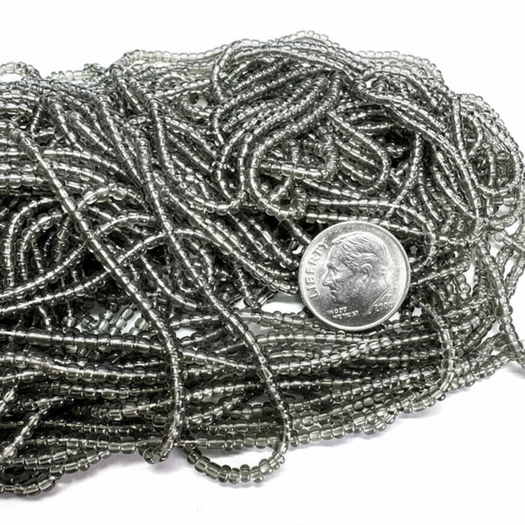 A close-up of a pile of metallic silver seed beads with a US dime coin placed on top for scale, set against a plain white background.