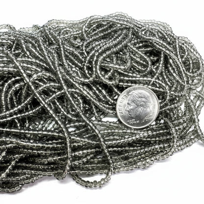 A close-up of a pile of metallic silver seed beads with a US dime coin placed on top for scale, set against a plain white background.