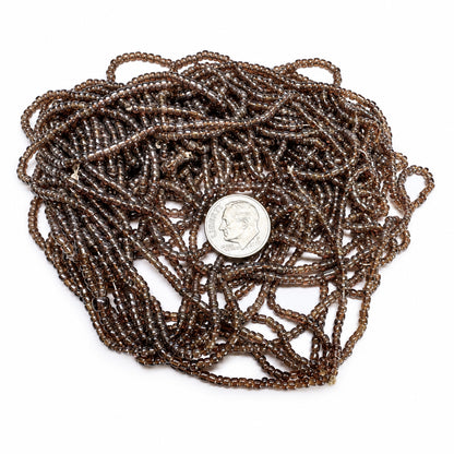 A coiled bundle of dark brown translucent glass seed beads with a silver-colored US dime placed in the center for scale, on a plain white background.