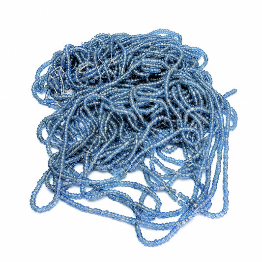 A pile of light blue faceted seed beads strung on clear cords, photographed on a plain white background.