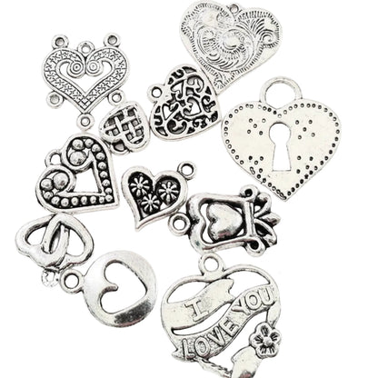A set of antique silver heart-shaped charms with various engravings, dots, keyhole details, and one charm reading 'I LOVE YOU,' arranged on a white background next to a US quarter for scale.