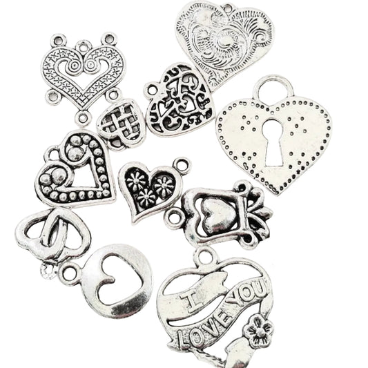 A set of antique silver heart-shaped charms with various engravings, dots, keyhole details, and one charm reading 'I LOVE YOU,' arranged on a white background next to a US quarter for scale.