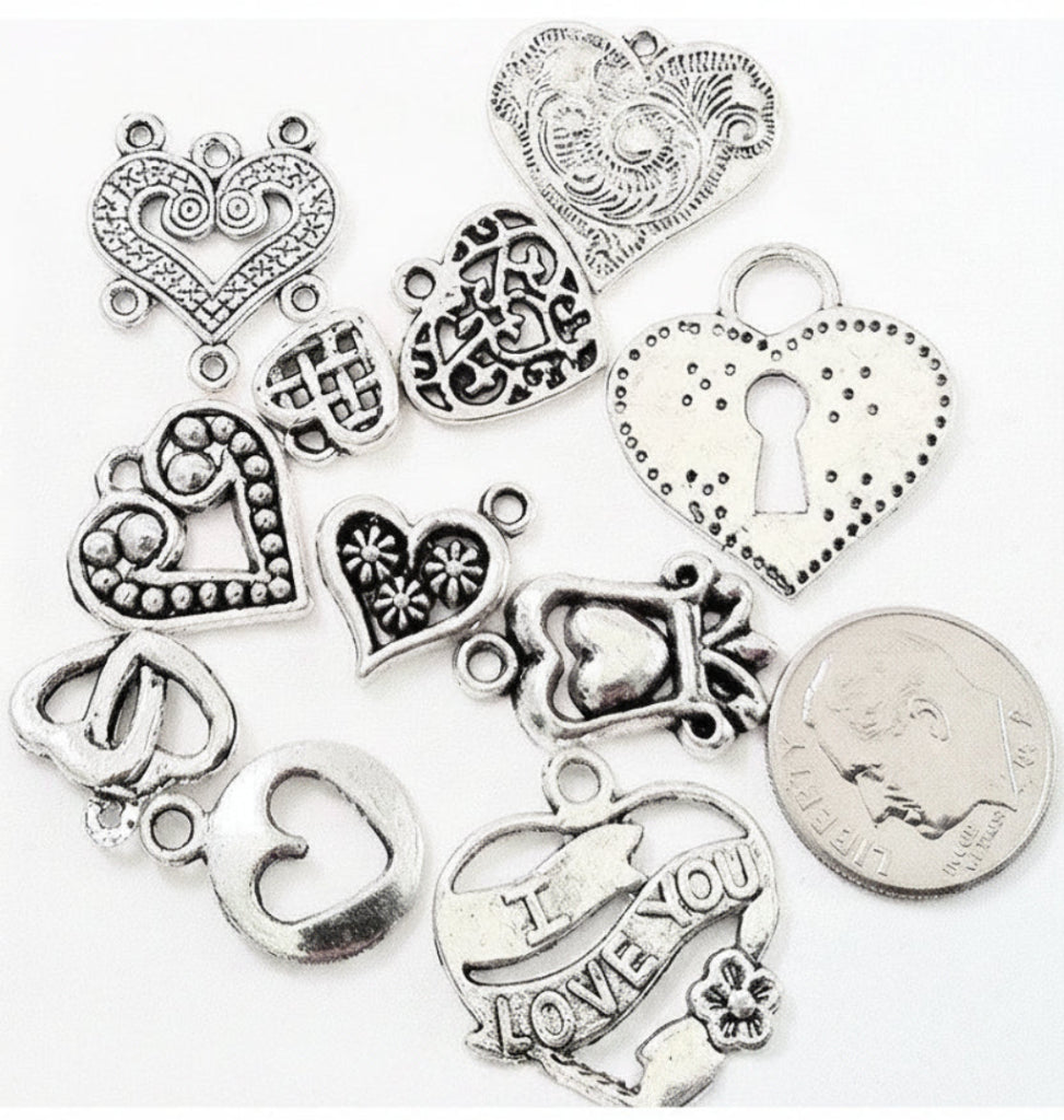 A set of silver-toned heart-shaped jewelry charms with various engraved and textured designs, displayed on a white background next to a US quarter coin for scale.