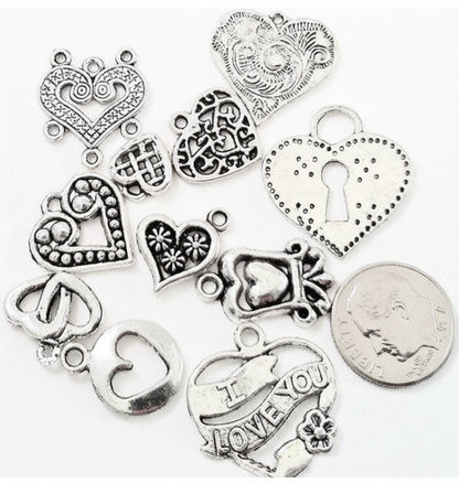 A set of silver-toned heart-shaped jewelry charms with various engraved and textured designs, displayed on a white background next to a US quarter coin for scale.