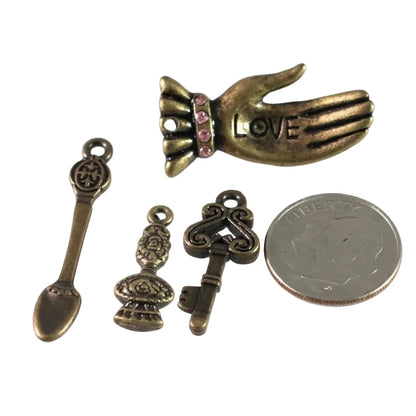 Four antique bronze-toned metal charms for jewelry making, including a hand with pink rhinestones and the word LOVE, a spoon-shaped charm, a decorative urn charm, and a key-shaped charm, displayed next to a US quarter for scale on a white background.
