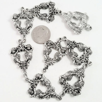 An ornate silver-toned chain bracelet with repeating heart-shaped links filled with floral and scrollwork details, shown on a white background with a DIME coin for scale.