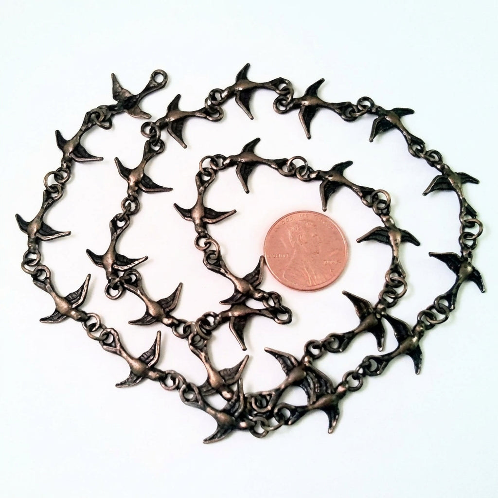 A antiqued gold metal chain necklace featuring repeating bird-shaped charms, displayed on a white background with a US quarter coin for scale.