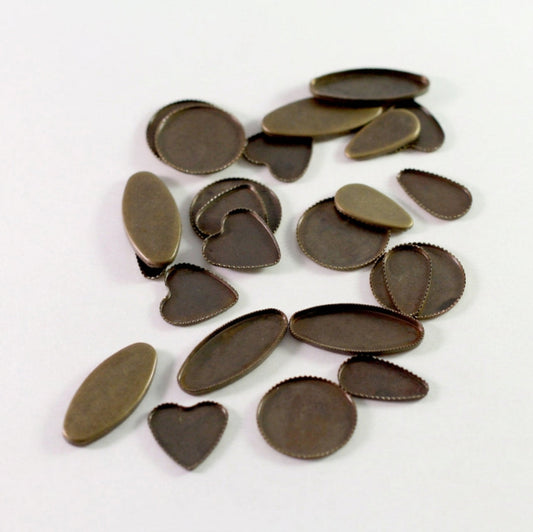 A pile of small metal jewelry findings or caps in an antique bronze finish, including oval, heart, and semi-circular pieces, scattered on a plain white background.