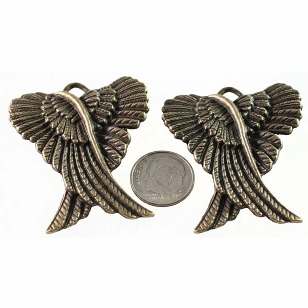 A pair of bronze angel wing charms shown next to a US quarter coin for scale, on a plain white background.