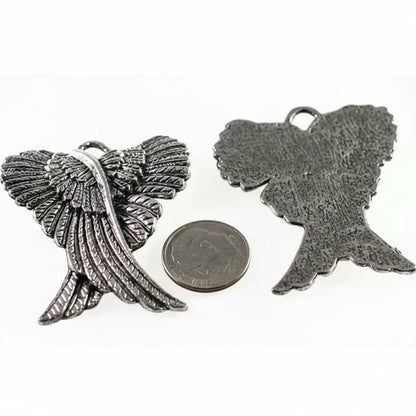 Two textured metal angel wing charms in a silver-tone finish, shown with a US quarter coin for scale on a plain white background.