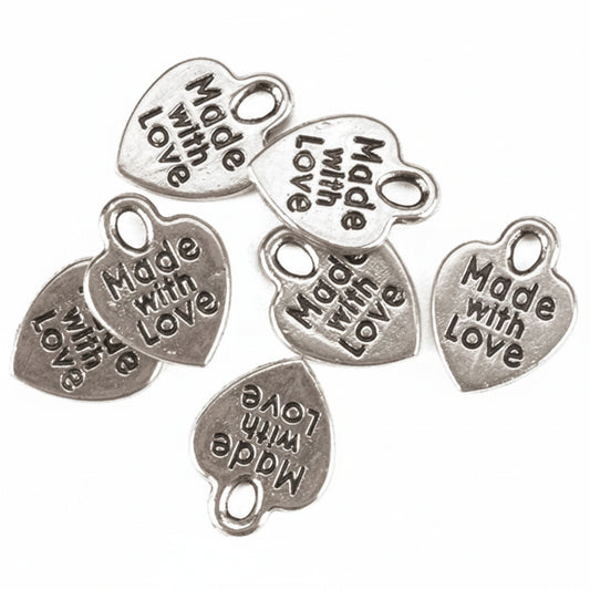 Seven silver heart-shaped jewelry charms with a loop at the top, each engraved with the phrase 'Made with Love' in a dark, raised font, arranged on a plain white background.