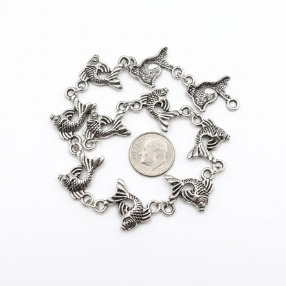 A silver-toned metal CHAIN featuring multiple dangling fish charms, arranged in a circle around a U.S. DIME