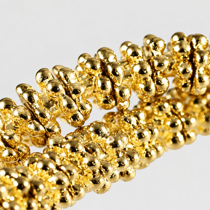 A close-up of a gold-colored beaded chain or bracelet with tightly packed, rounded metallic beads on a plain light gray background.