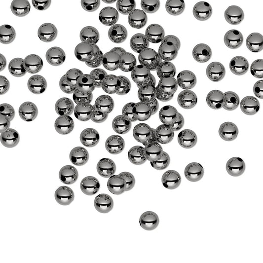 A scattered collection of small, shiny metallic gunmetal beads with a central hole, photographed on a solid white background.