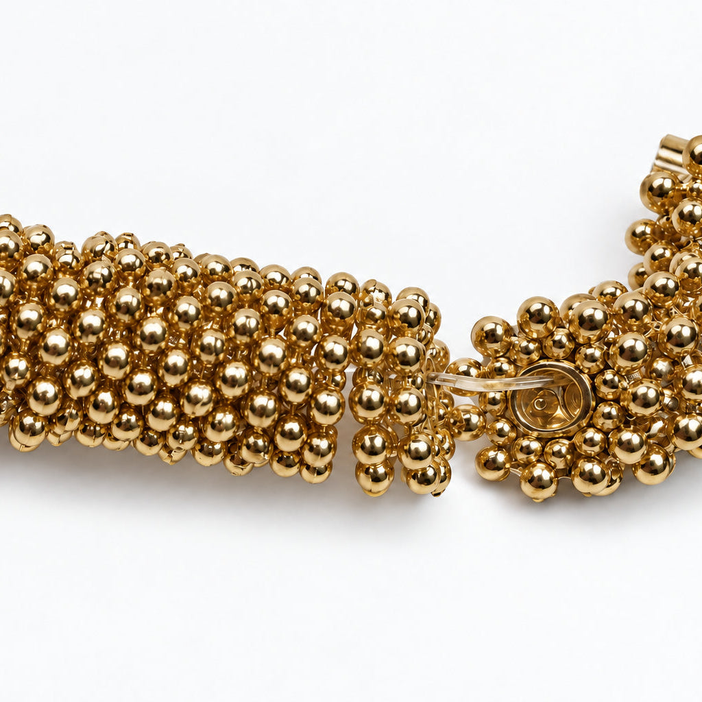 A close-up of a gold beaded strand or bracelet component made of many small metallic round beads, photographed on a plain white background.
