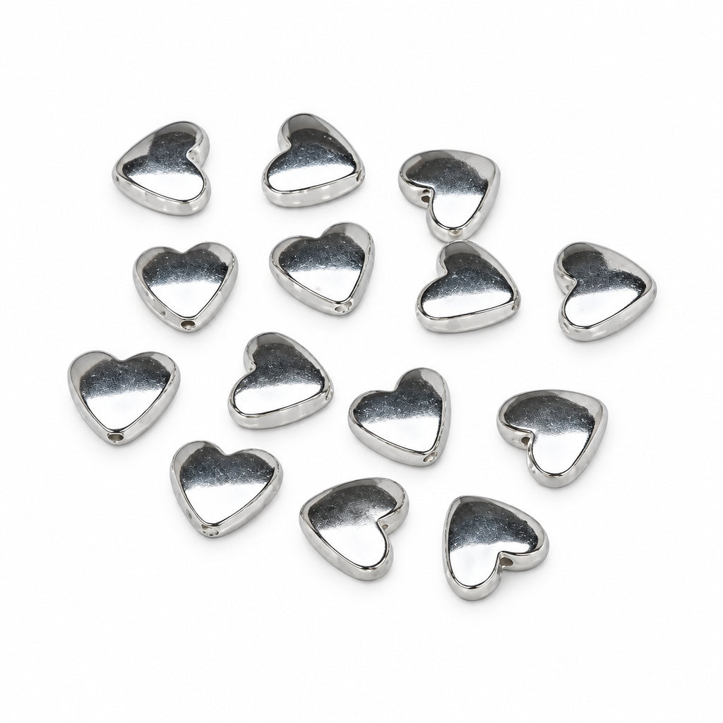 A group of small, polished silver heart-shaped beads scattered on a plain white background.