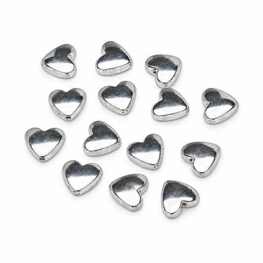 A group of small, polished silver heart-shaped beads scattered on a plain white background.