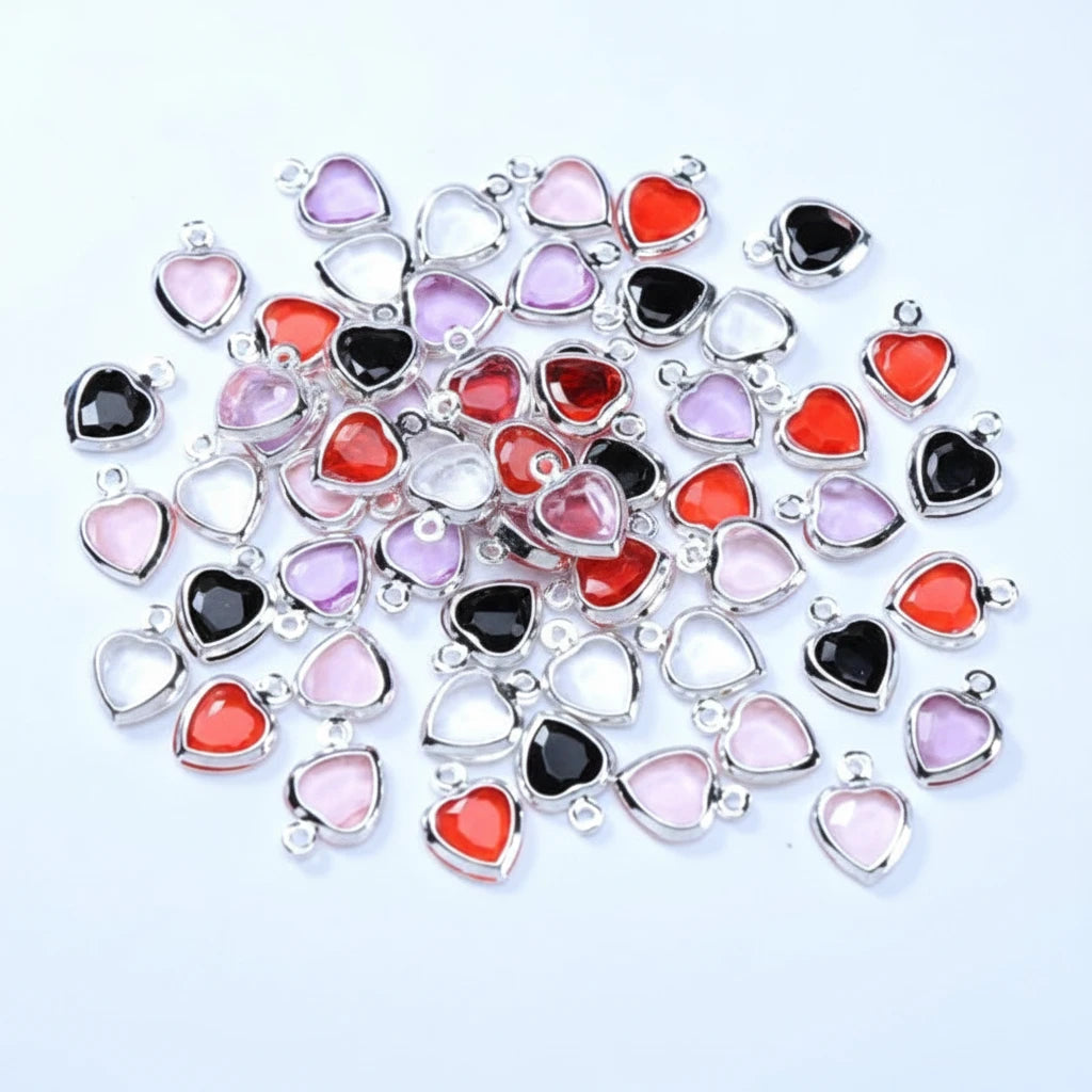 A pile of heart-shaped jewelry charms with silver-toned metal borders and faceted stones in black, red, pink, and lavender, arranged on a plain white background.