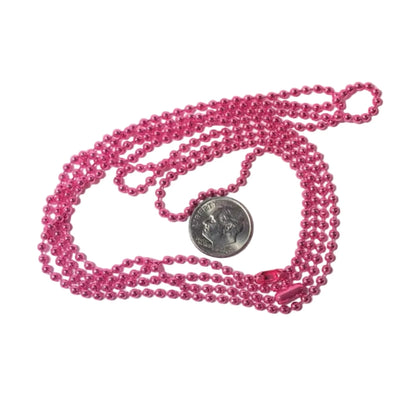 A pink beaded necklace with a small silver coin placed on top for scale, photographed on a plain white background.