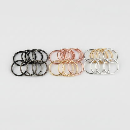 Three sets of thin metal O-rings or spacer rings arranged side by side on a light gray background. The left set is black and dark gray, the middle set is rose gold and gold, and the right set is silver and gold.