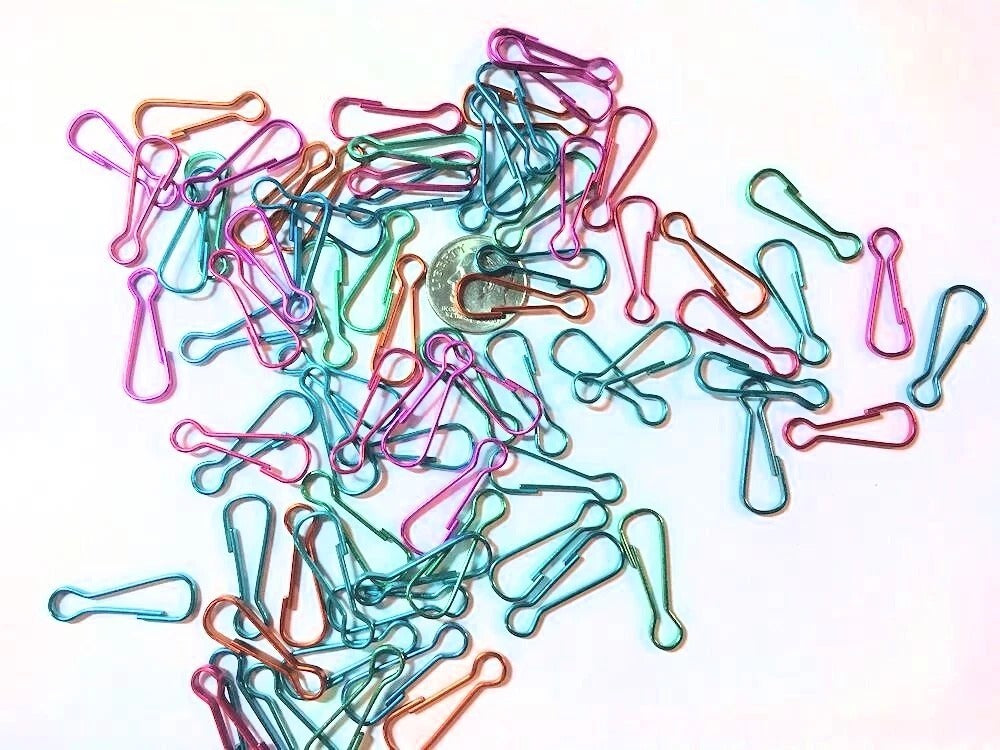 A set of small metal carabiners in pastel colors including light blue, mint green, peach, pink, and lavender, scattered on a plain white background.