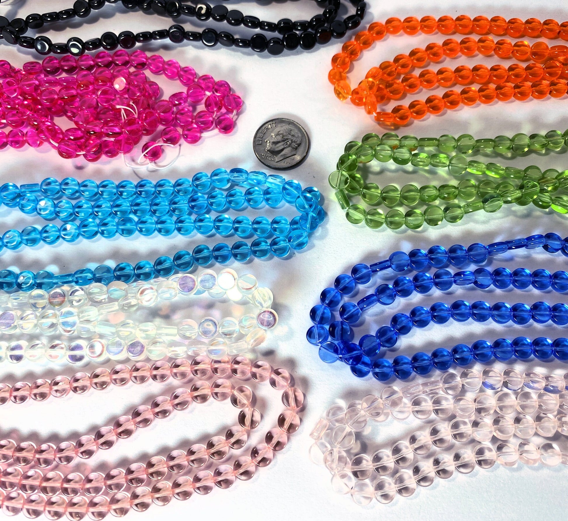 Assorted colorful beads on a white surface with a coin for size reference.