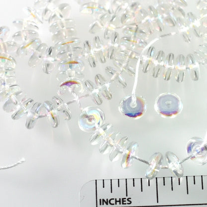 Clear acrylic spool beads with an iridescent finish, shown on a white background with a 1-inch ruler for scale.