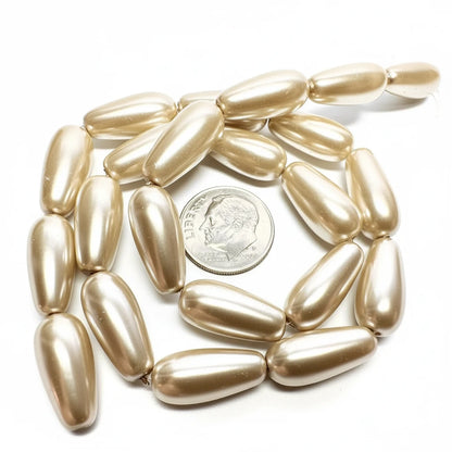 A strand of metallic gold teardrop-shaped beads, shown with a US quarter coin for scale on a plain white background.