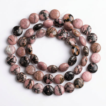 A strand of polished round gemstone beads in pink, brown, black, and white marbled patterns, arranged on a plain white background.