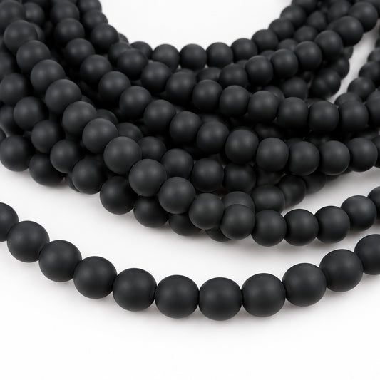 Matte black round beads strung on cords, shown in multiple overlapping strands against a plain white background.