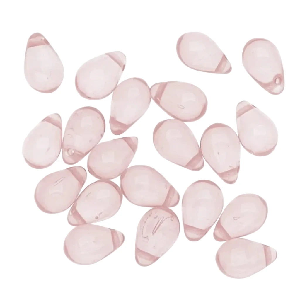 A group of small, teardrop-shaped translucent pink glass beads scattered on a plain white background.