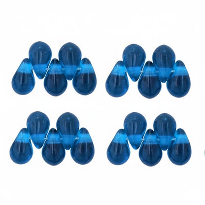 Six pairs of translucent blue teardrop-shaped beads arranged in a grid on a plain white background.